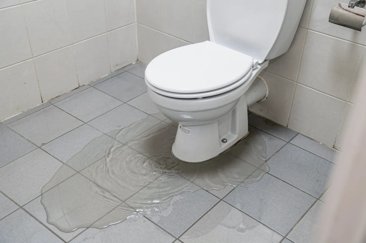 Banheiro azulejado com vaso e água no piso