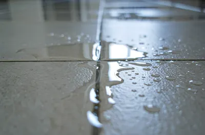 Água surgindo entre os azulejos do piso por vazamento oculto