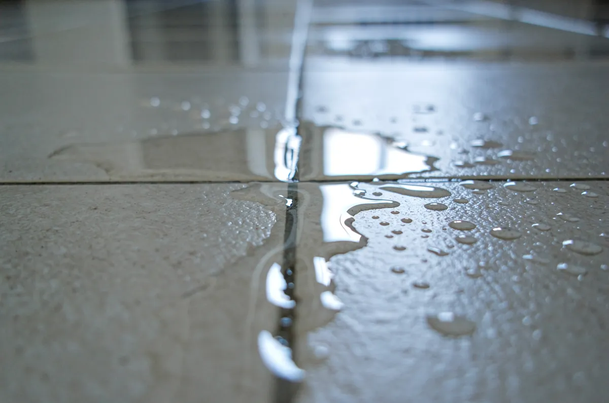 Água surgindo entre os azulejos do piso por vazamento oculto