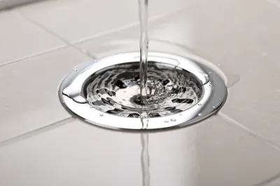 Ralo cromado de chuveiro com água escoando no piso