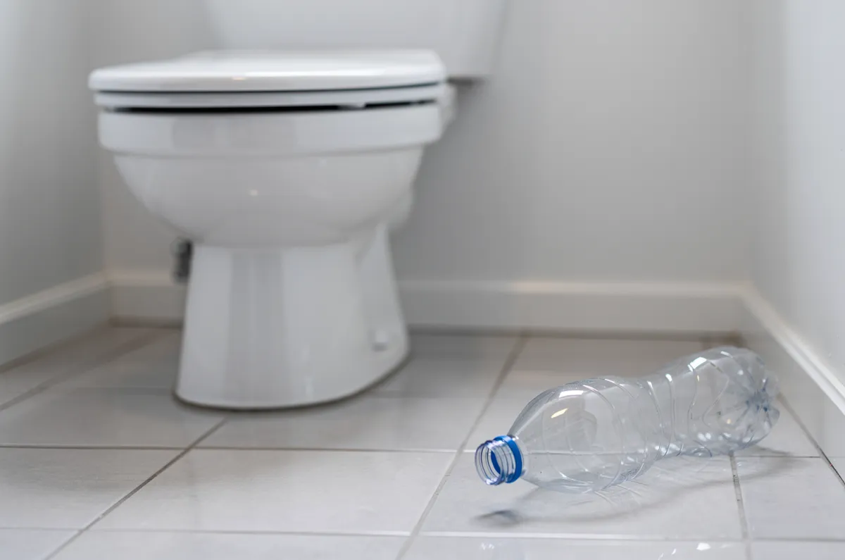 Garrafa PET no piso ao lado de uma privada branca