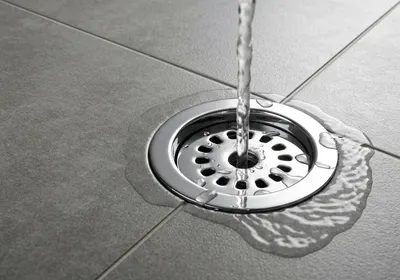 Ralo cromado de banheiro com água escoando no piso