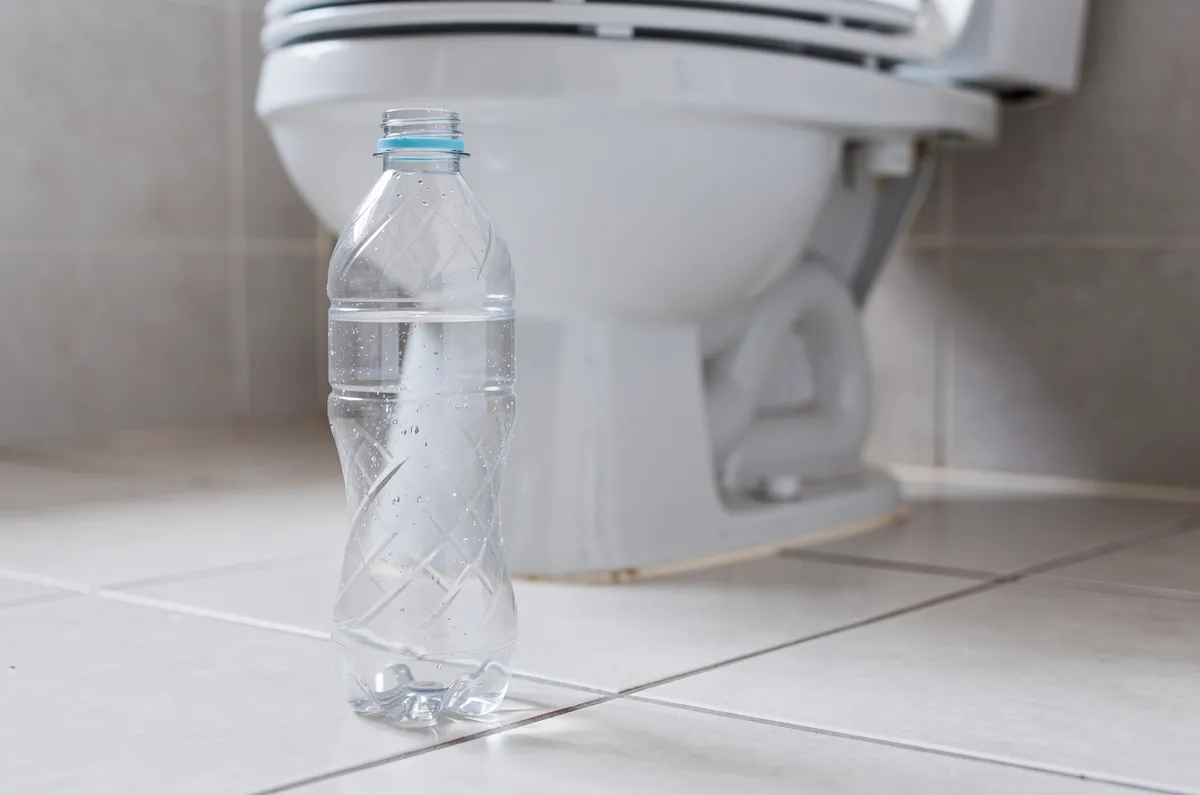 Garrafa PET no piso do banheiro ao lado de um vaso
